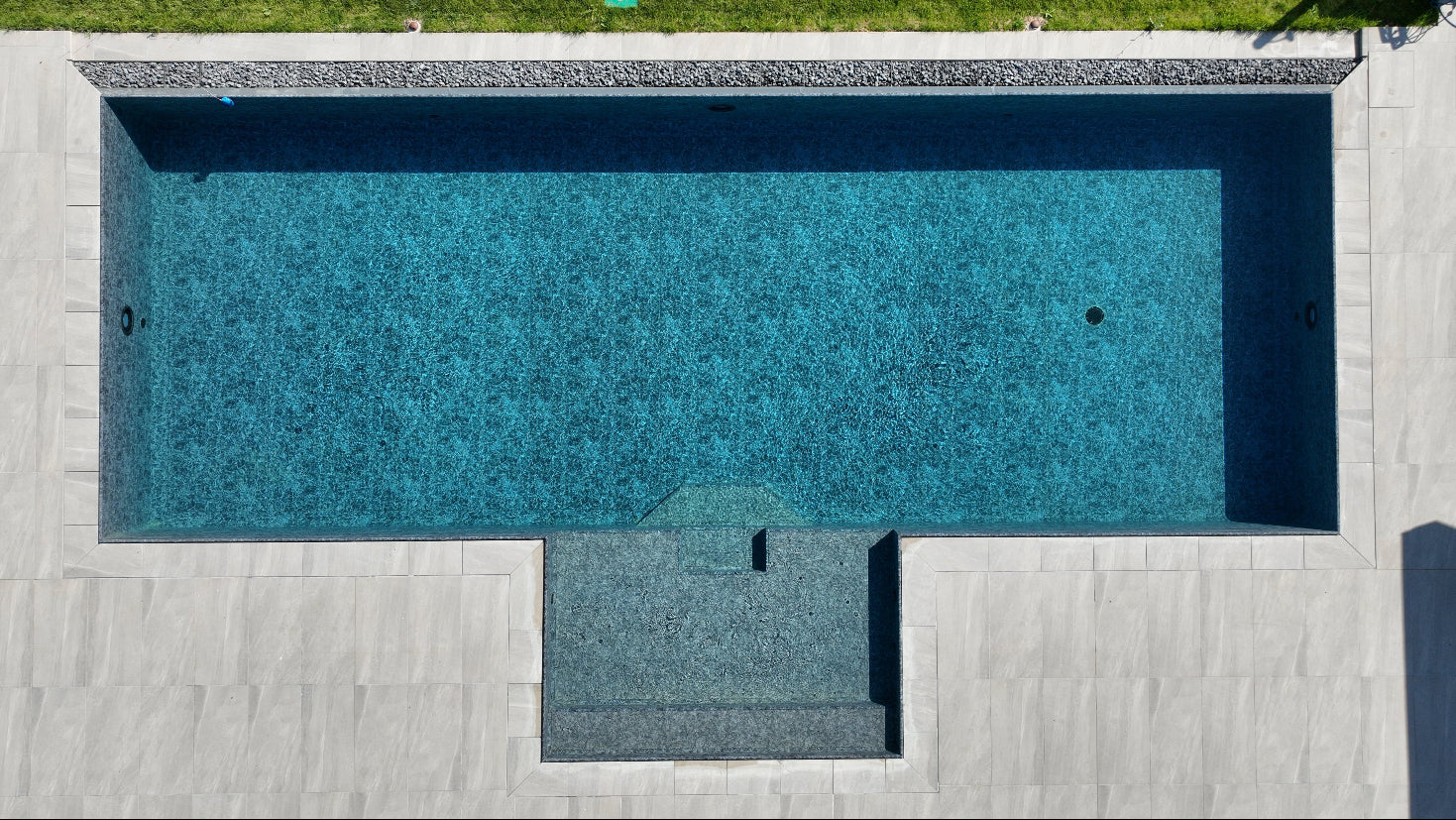 Piscina a Sfioro by Zavatti senza vasca di compenso, rivestimento nero marmorizzato e lato lungo con sassi decorativi