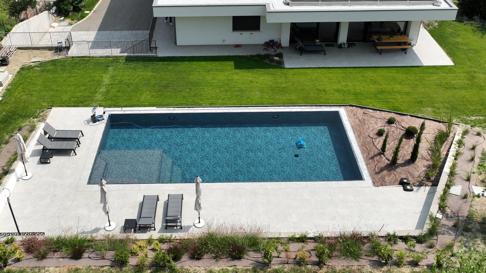 Piscina a Sfioro senza vasca di compenso dal design moderno, contrasto tra rivestimento nero marmorizzato e pavimento grigio chiaro, vaschette decorative porta sassi su due lati