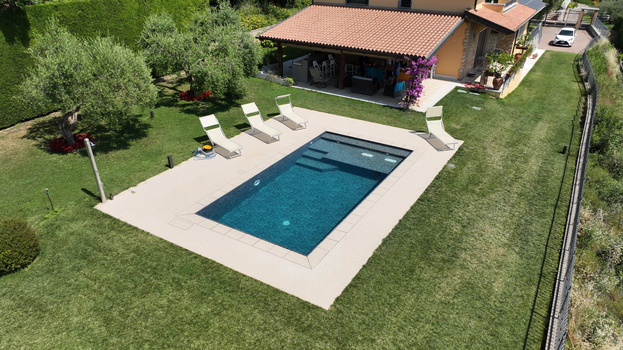 Piscina a Sfioro senza vasca di compenso nera marmorizzata rettangolare con spiaggia interna in testa e zona relax con piastre blower idromassaggio by Zavatti Piscine
