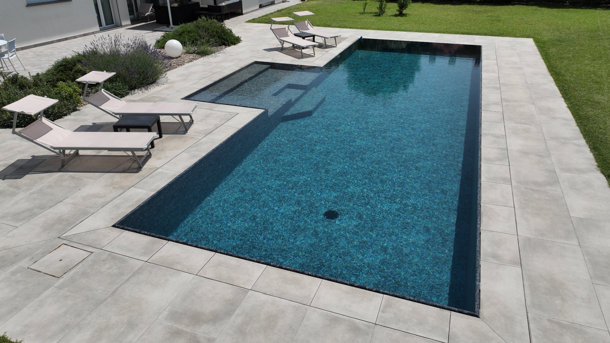 Piscina a sfioro autopulente senza vasca di compenso con spiaggia centrale e rivestimento nero marmorizzato, pavimento grigio chiaro