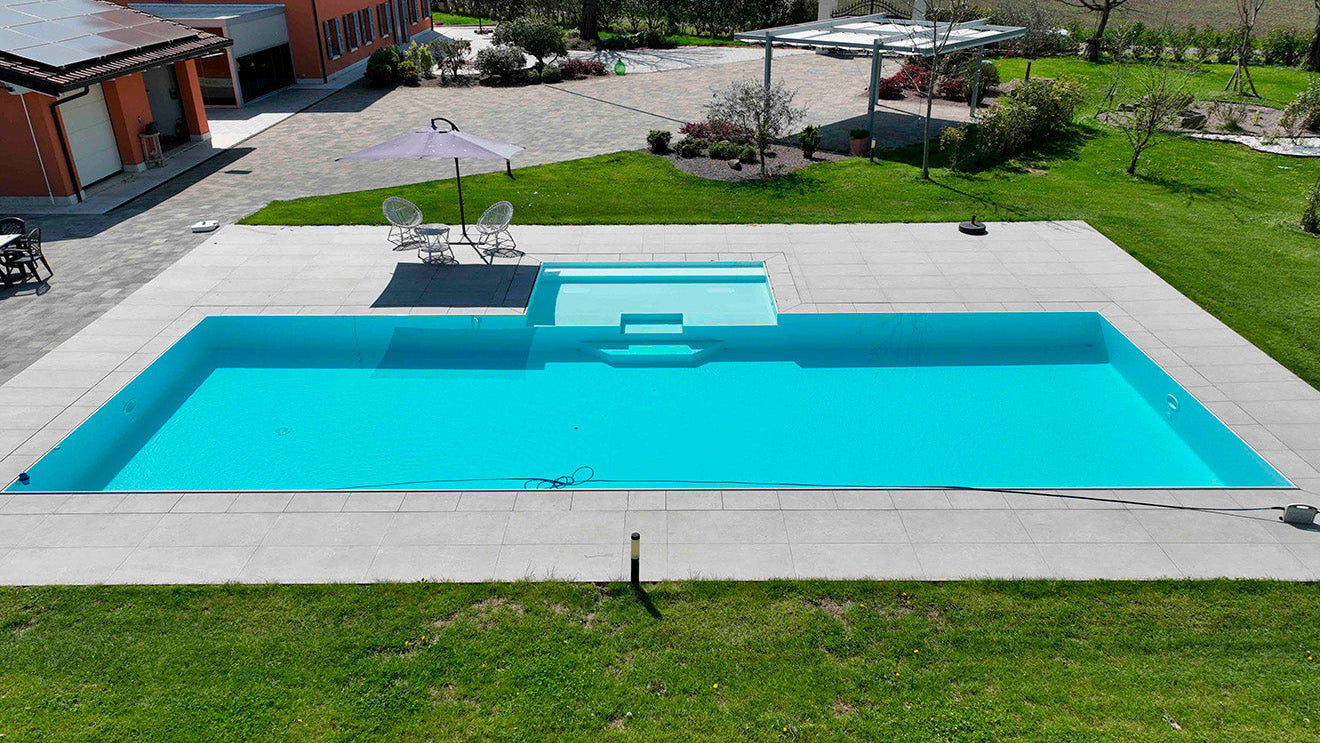 piscina a sfioro senza vasca di compenso colore bianco e grigio chiaro, con spiaggia esterna centrale e blower per idromassaggio