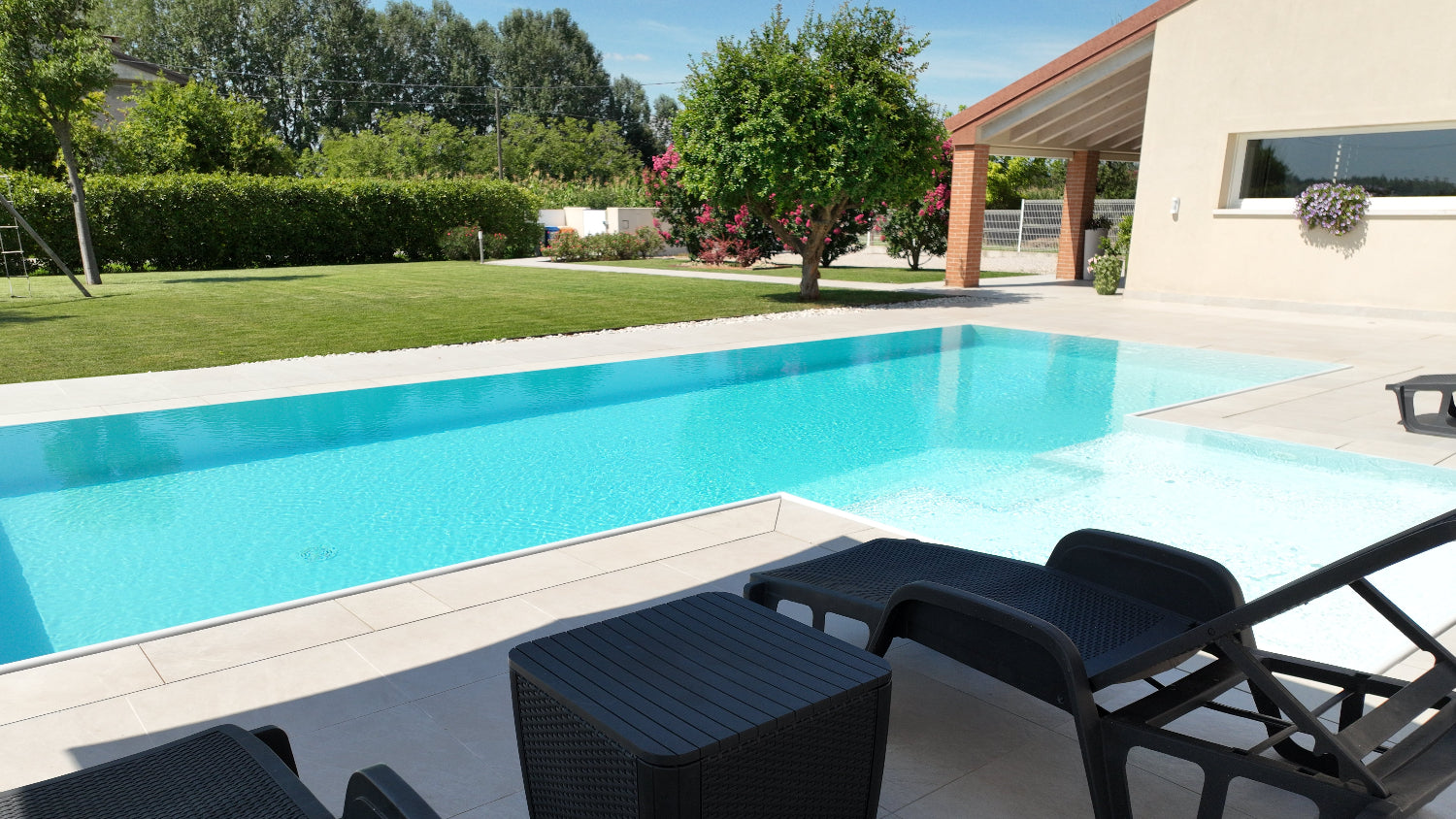Piscina a sfioro con rivestimento chiaro, realizzata a San Biagio di Callalta, Treviso con spiaggia centrale giardino in fiore