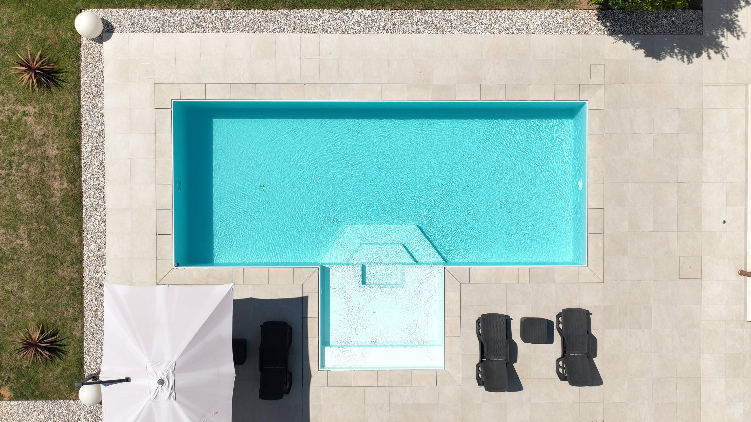Piscina a sfioro con rivestimento chiaro, realizzata a San Biagio di Callalta, Treviso con spiaggia centrale giardino in fiore moderno