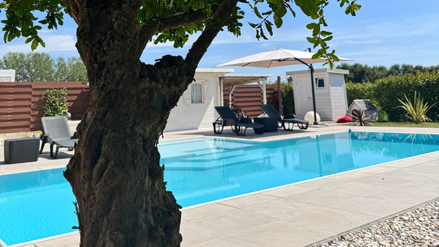 Piscina a sfioro con rivestimento grigio chiaro e spiaggia bianca zona prendisole