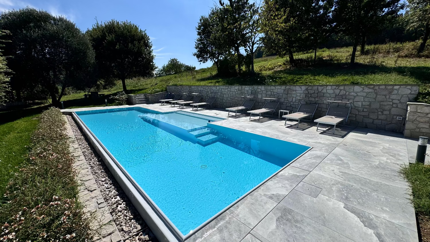 Piscina a sfioro con spiaggia centrale semi esterna rivestimento grigio chiaro