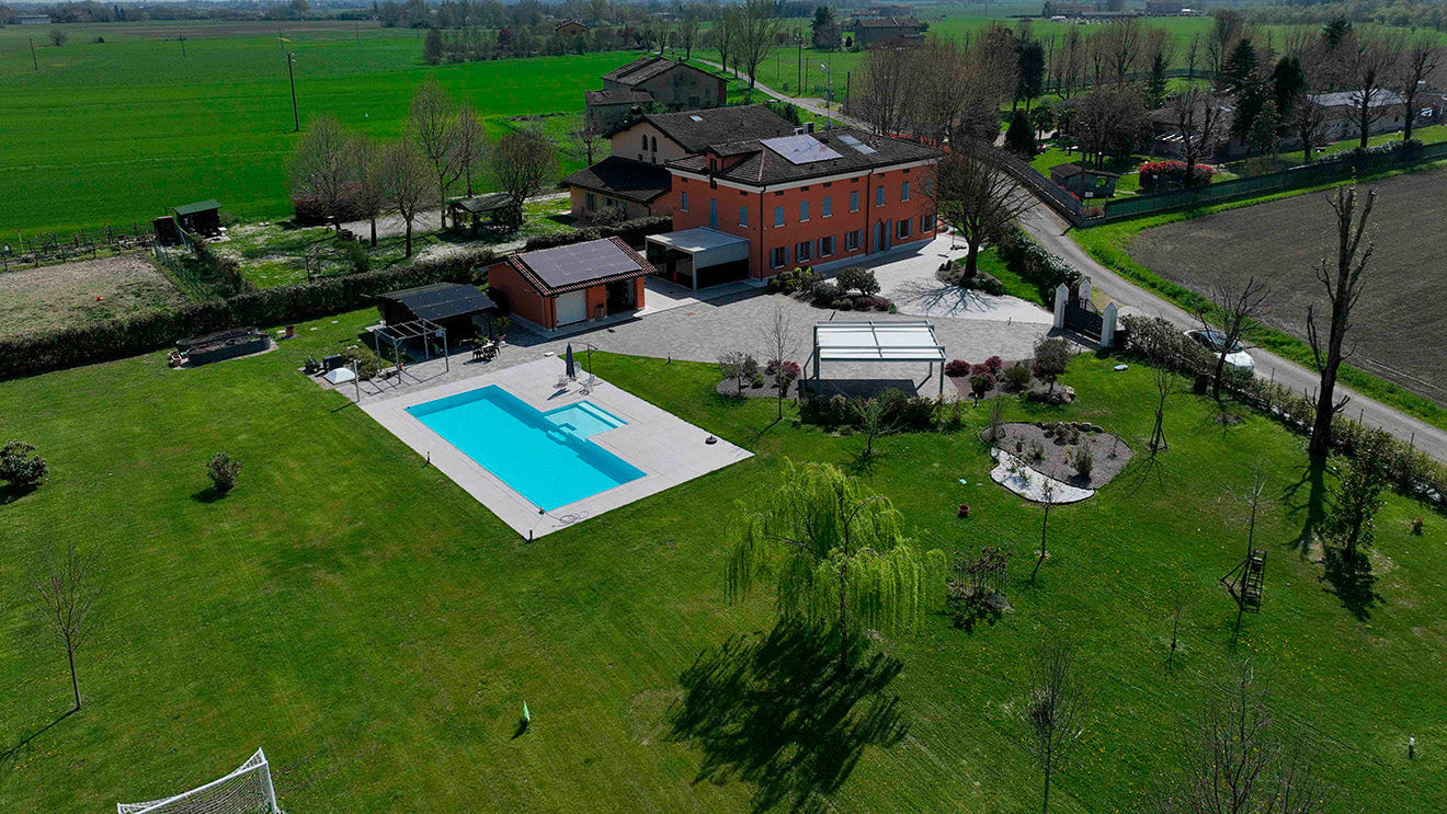 Piscina a sfioro rettangolare senza vasca di compenso con spiaggia esterna centrale, immersa nel verde a Marzaglia