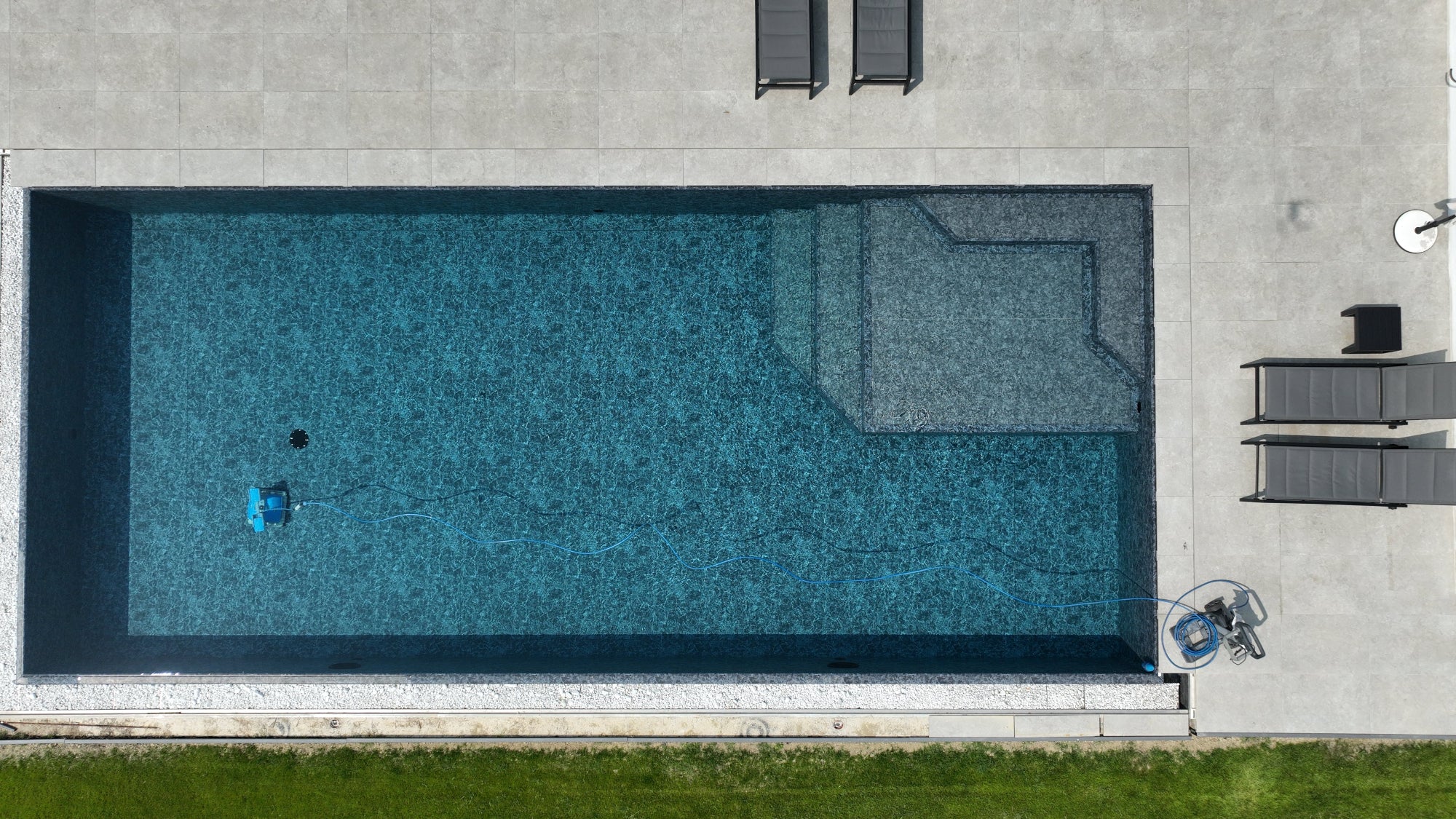 Piscina a sfioro rettangolare con zona relax interna angolare e rivestimento nero marmorizzato, griglie con vaschette rimepite di sassi decorativi su due lati effetto cascata a Castellarano (RE)