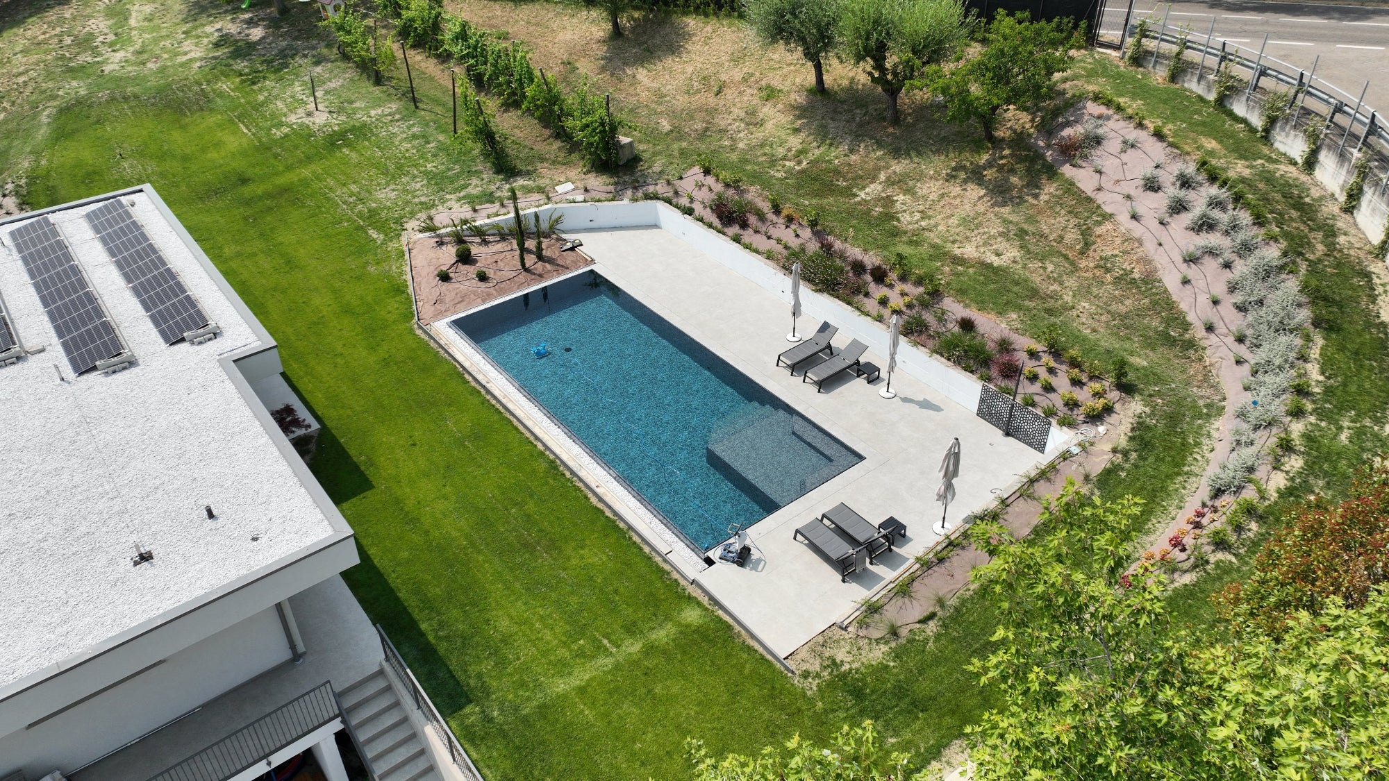 Piscina a sfioro rettangolare senza vasca di compenso con bagnasciuga interno angolare e rivestimento nero effetto marmorizzato, vaschette decorative con sassi su due lati a Castellarano (RE)