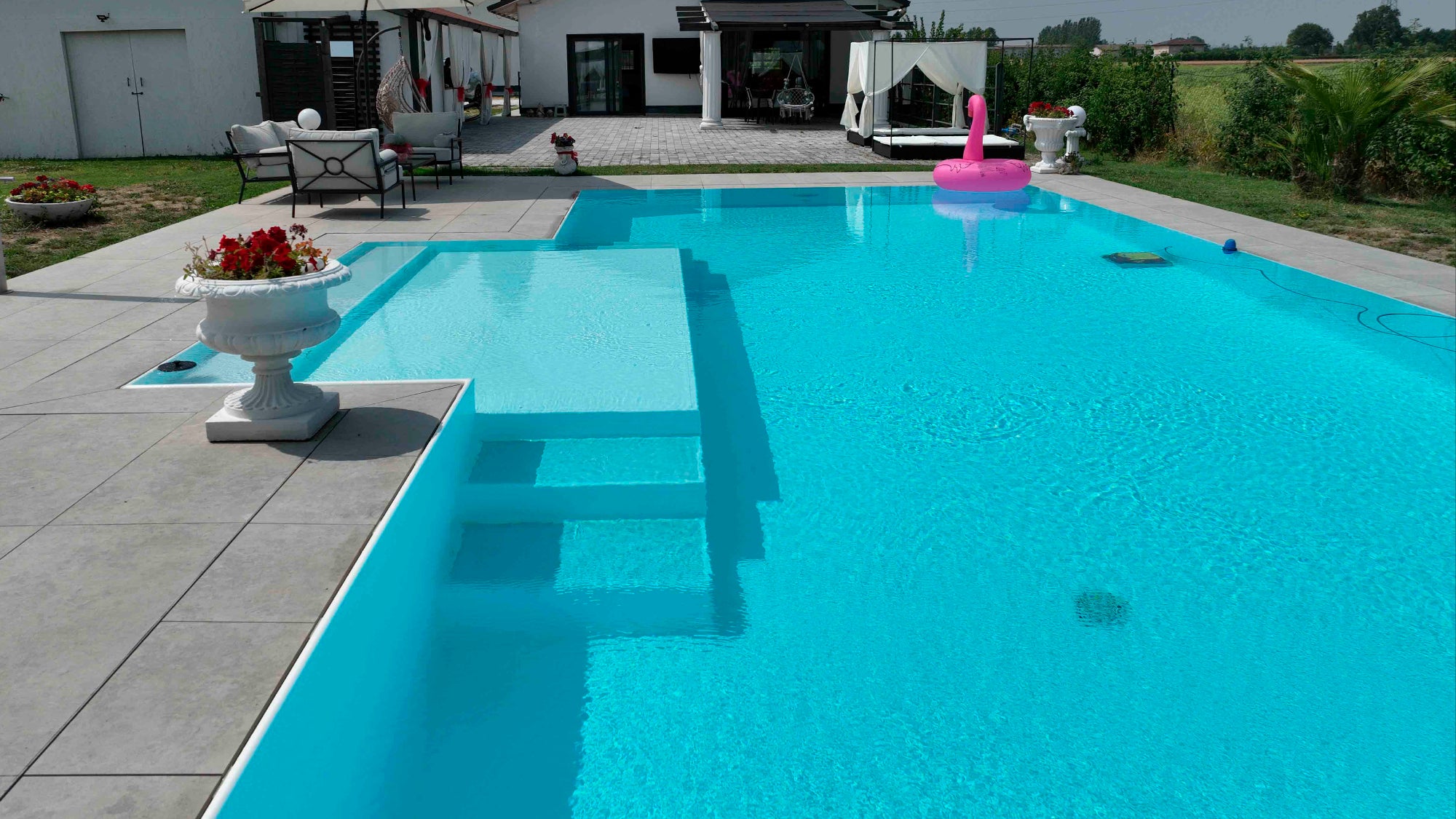 Piscina a sfioro senza vasca di compenso con bagnasciuga semiesterno centrale e doppi gradini, rivestimento bianco