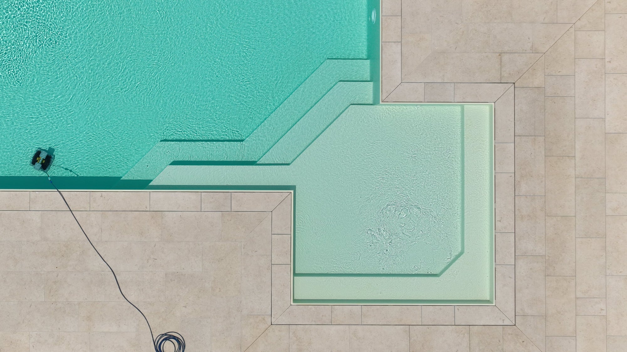 Piscina a sfioro senza vasca di compenso con spiaggia angolare esterna con gradinate particolari. Rivestimento sabbia e pavimento beige.