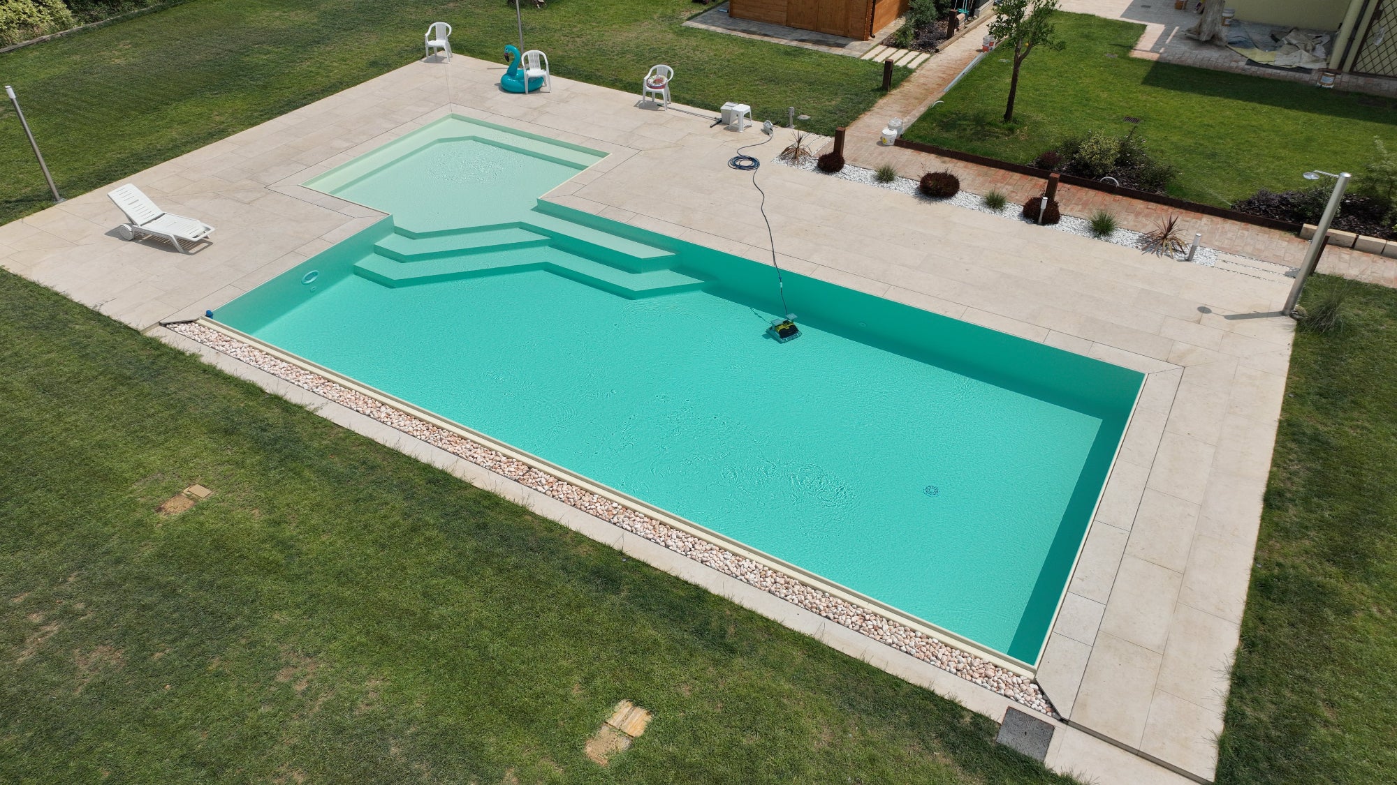 Piscina a sfioro senza vasca di compenso con spiaggia angolare esterna e vaschette con sassi decorativi, rivestimento sabbia a Spilamberto