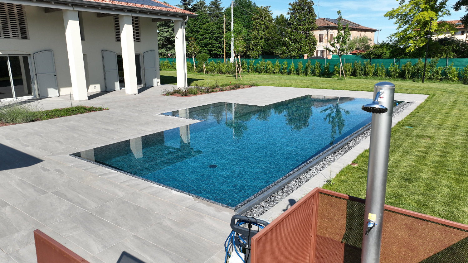 Piscina a sfioro senza vasca di compenso con spiaggia esterna centrale e rivestimento nero marmorizzato. Lato a cascata con vaschette inox per sassi decorativi by Zavatti 