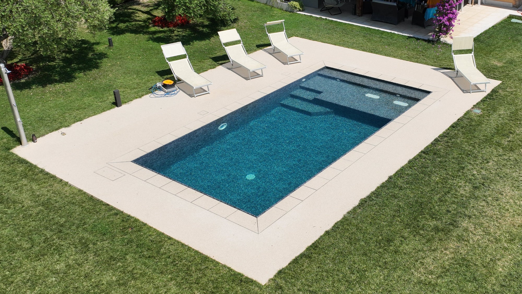 Piscina a sfioro senza vasca di compenso con spiaggia interna per tutta la larghezza, con piastre idromassaggio e rivestimento nero marmorizzato a Cavaion Veronese 