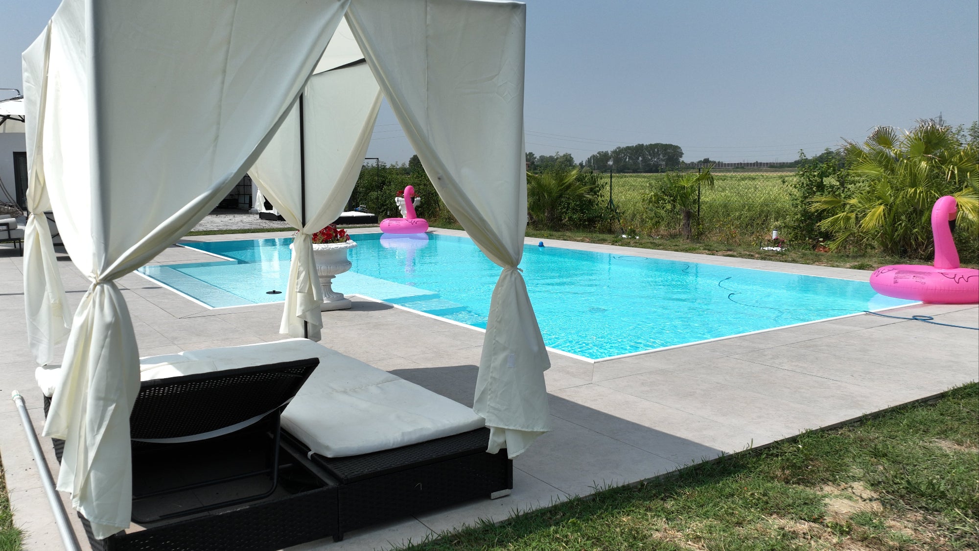 Piscina a sfioro senza vasca di compenso con spiaggia semiesterna centrale rivestimento bianco