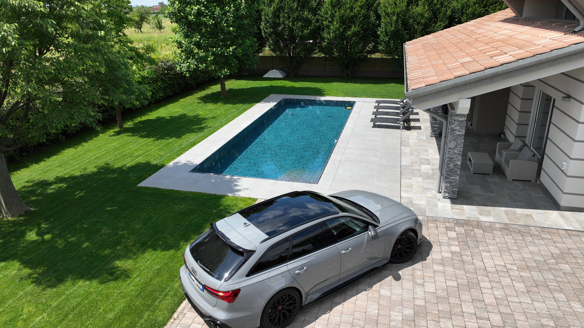 Piscina a sfioro senza vasca di compenso dalla forma rettangolare e rivestimento nero marmorizzato, immersa nel verde a Cittadella (PD)