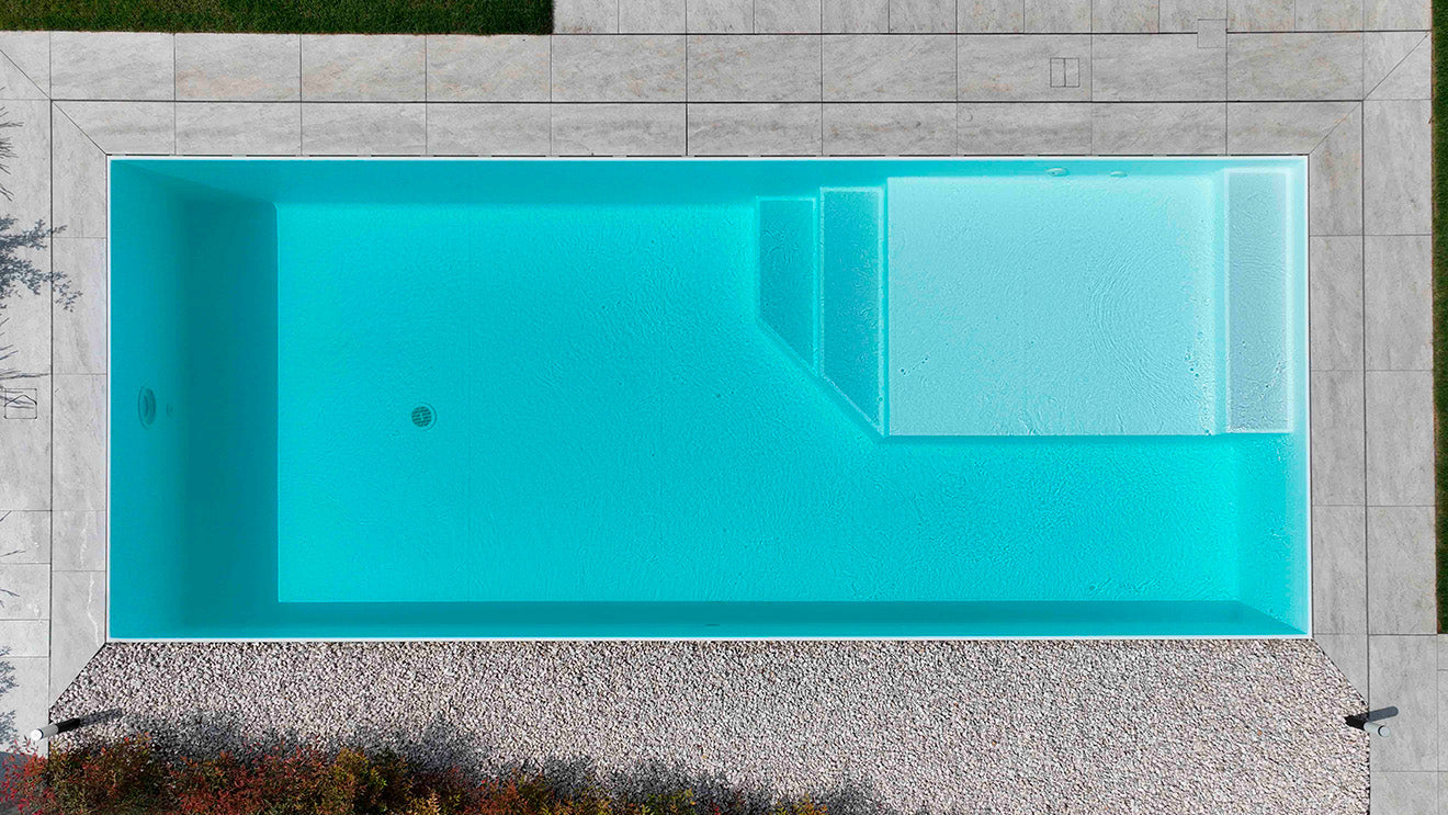 Piscina rettangolare a sfioro senza vasca di compenso rivestimento bianco zona relax interna in angolo