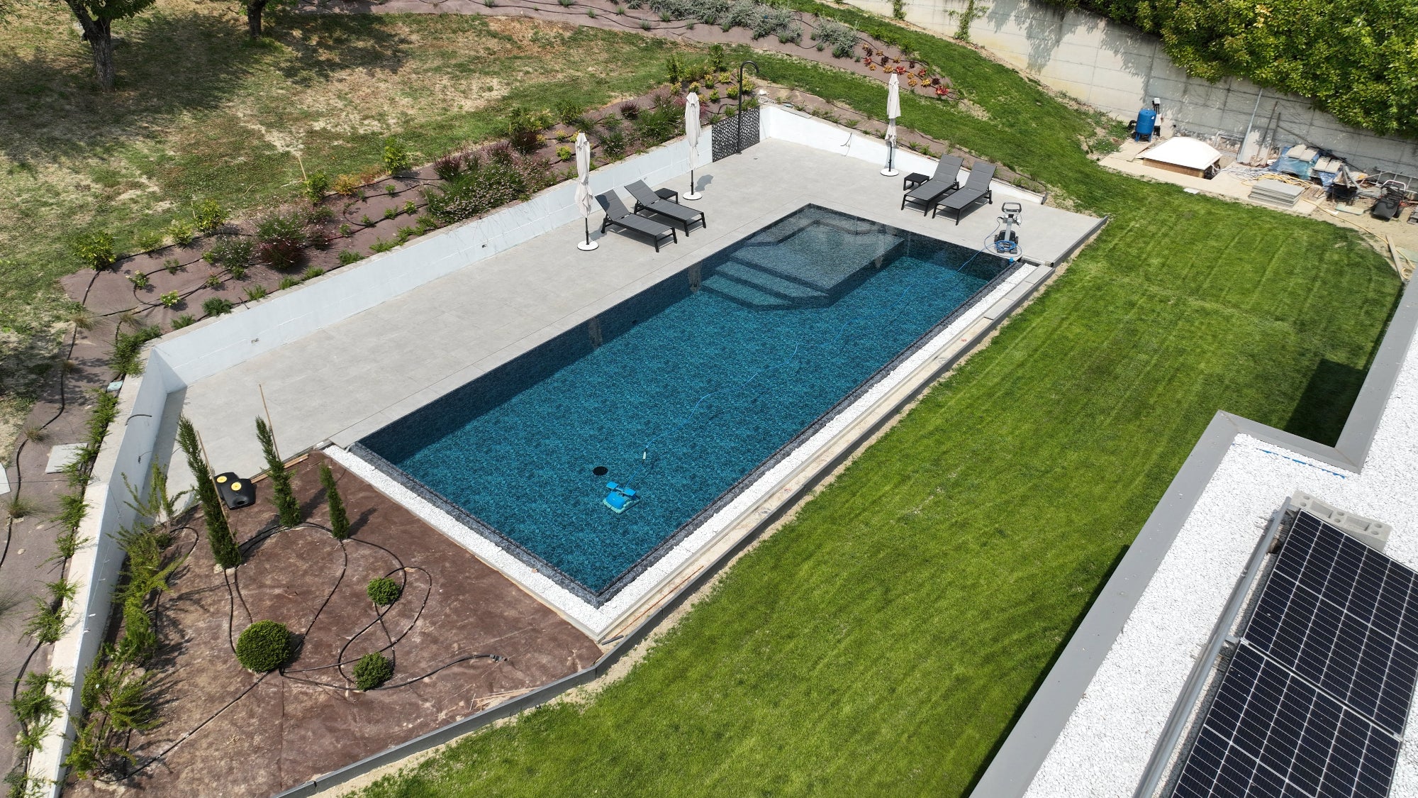 Piscina sfioro by Zavatti senza vasca di compenso dal design moderno ed accattivante, zona relax interna in angolo e rivestimento nero effetto marmo, vaschette con sassi decorativi bianchi su due lati 