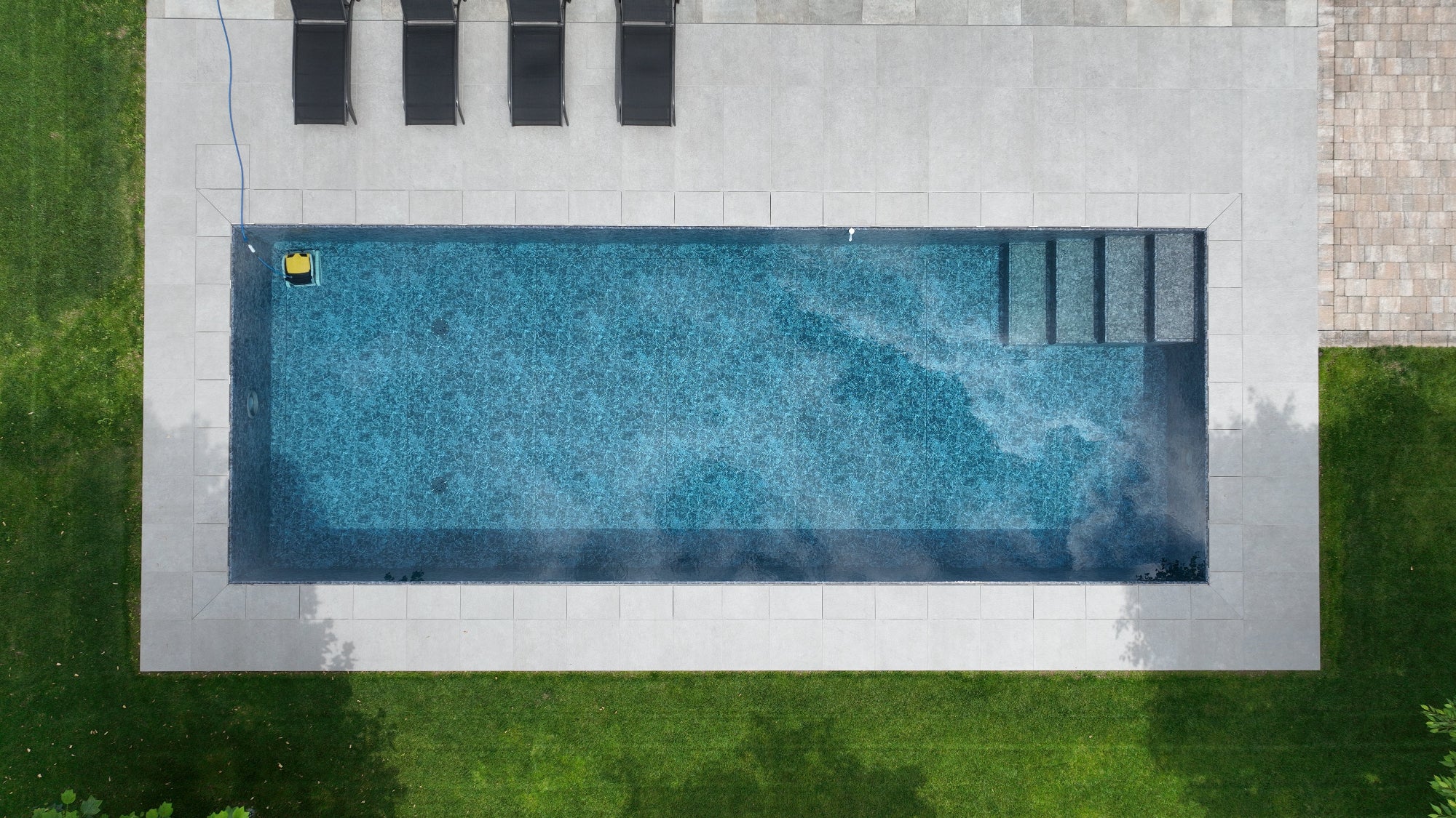 Piscina sfioro rettangolare con gradini interni senza vasca di compenso, rivestimento nero marmorizzato. Sfioro effetto specchio, riprese drone Cittadella (PD)