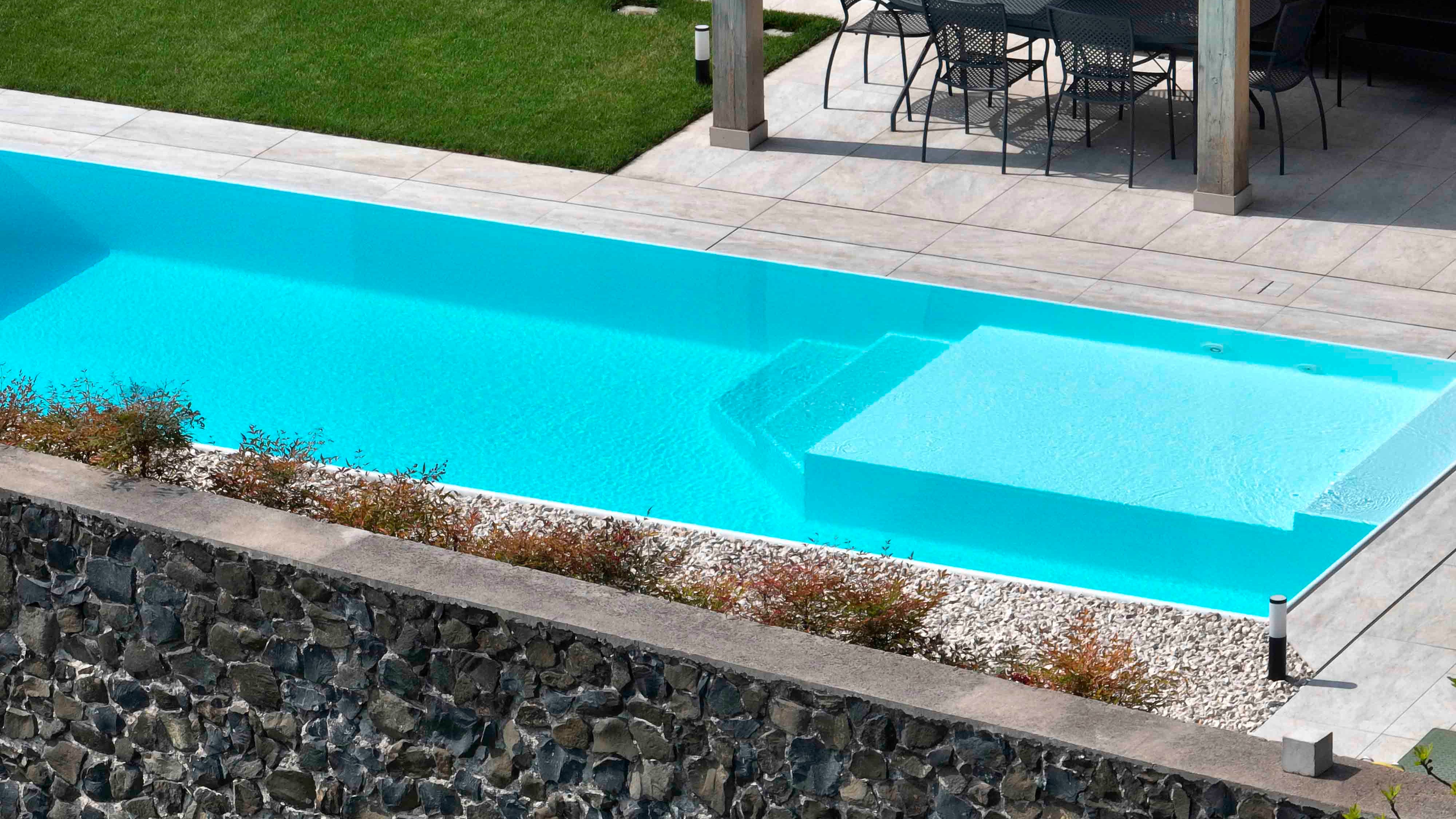 Piscina sfioro rettangolare con spiaggia interna in angolo, rivestimento chiaro e vaschette in acciaio per sassi decorativi sul lato lungoa Monteforte D'Alpone