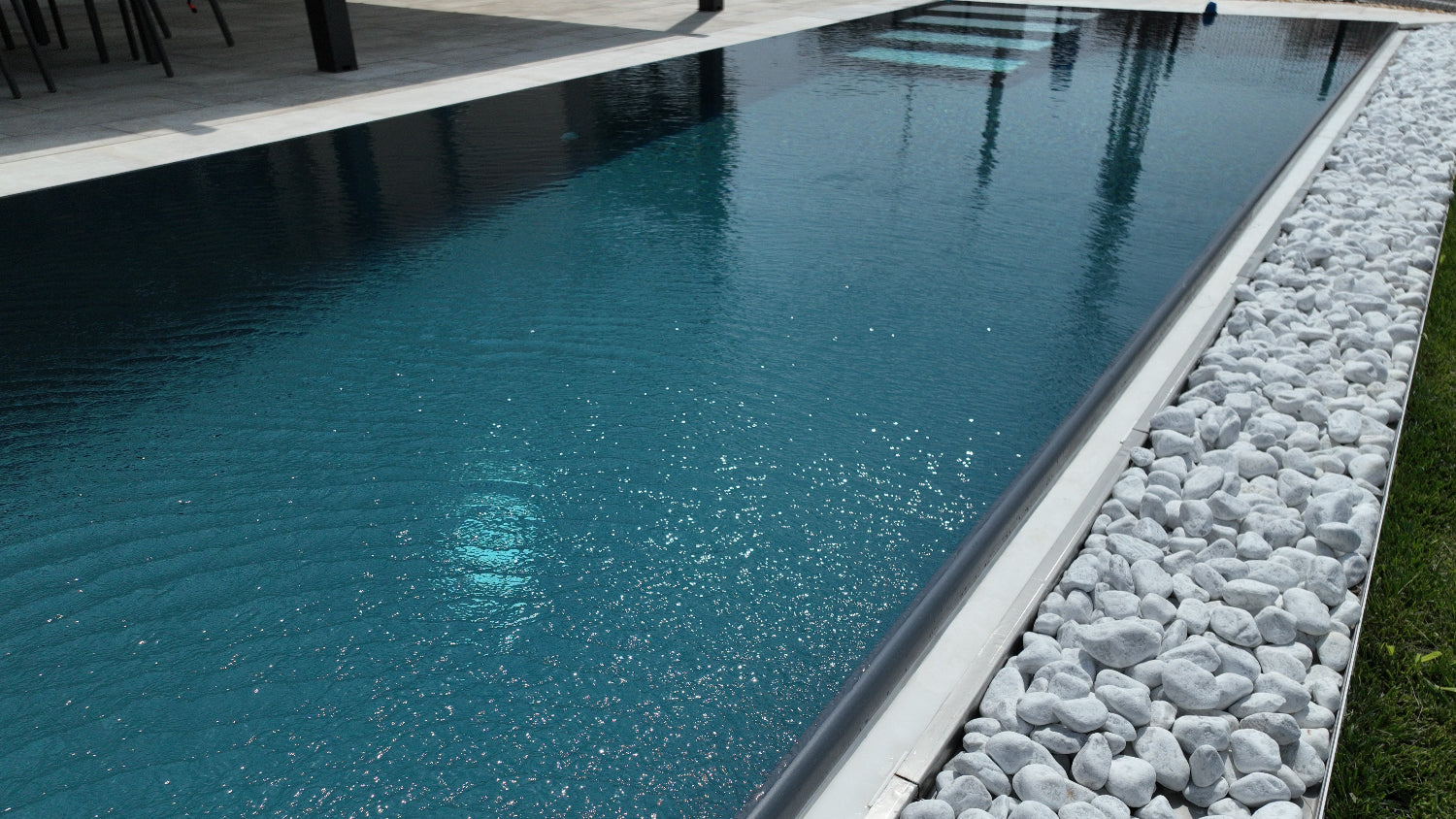 dettaglio piscina a sfioro con vaschetta sfioro con sassi decorativi