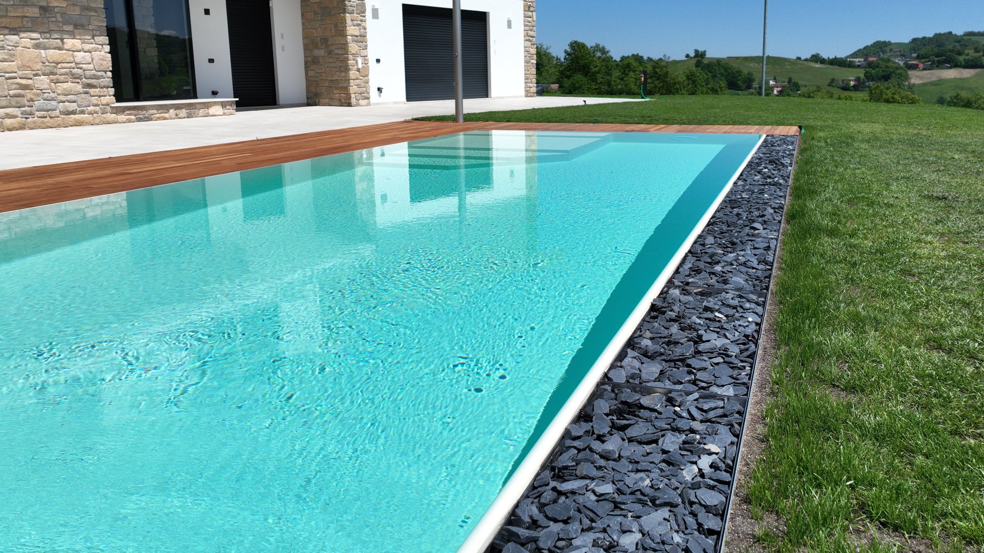 dettaglio piscina sfioro senza vasca di compenso con rivestimento color sabbia e vaschette inox con pietre di ardesia