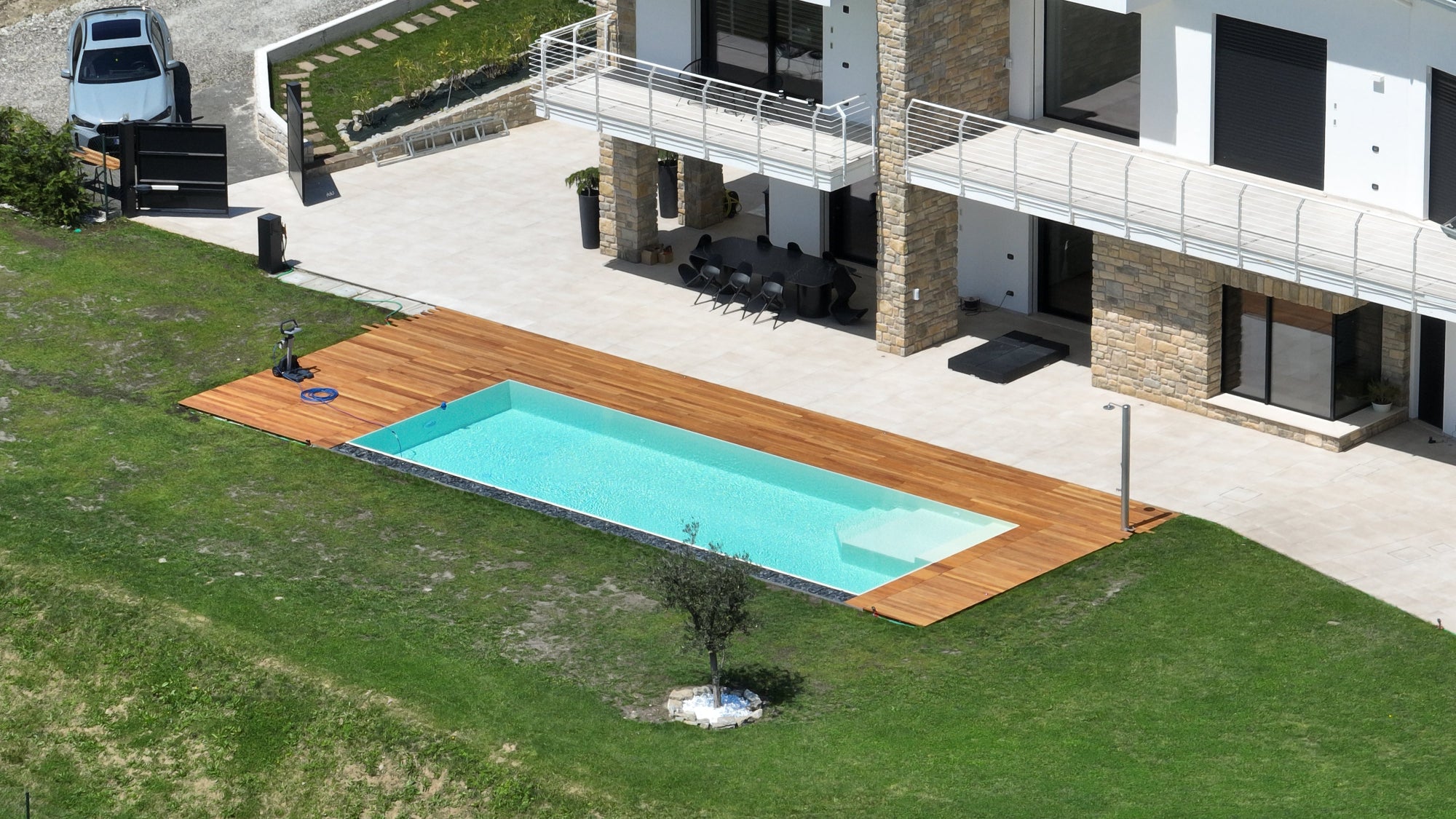 piscina a sfioro con bagnasciuga interno ad angolo color sabbia e vaschette con sassi decorativi su lato lungo, pavimento in legno 
