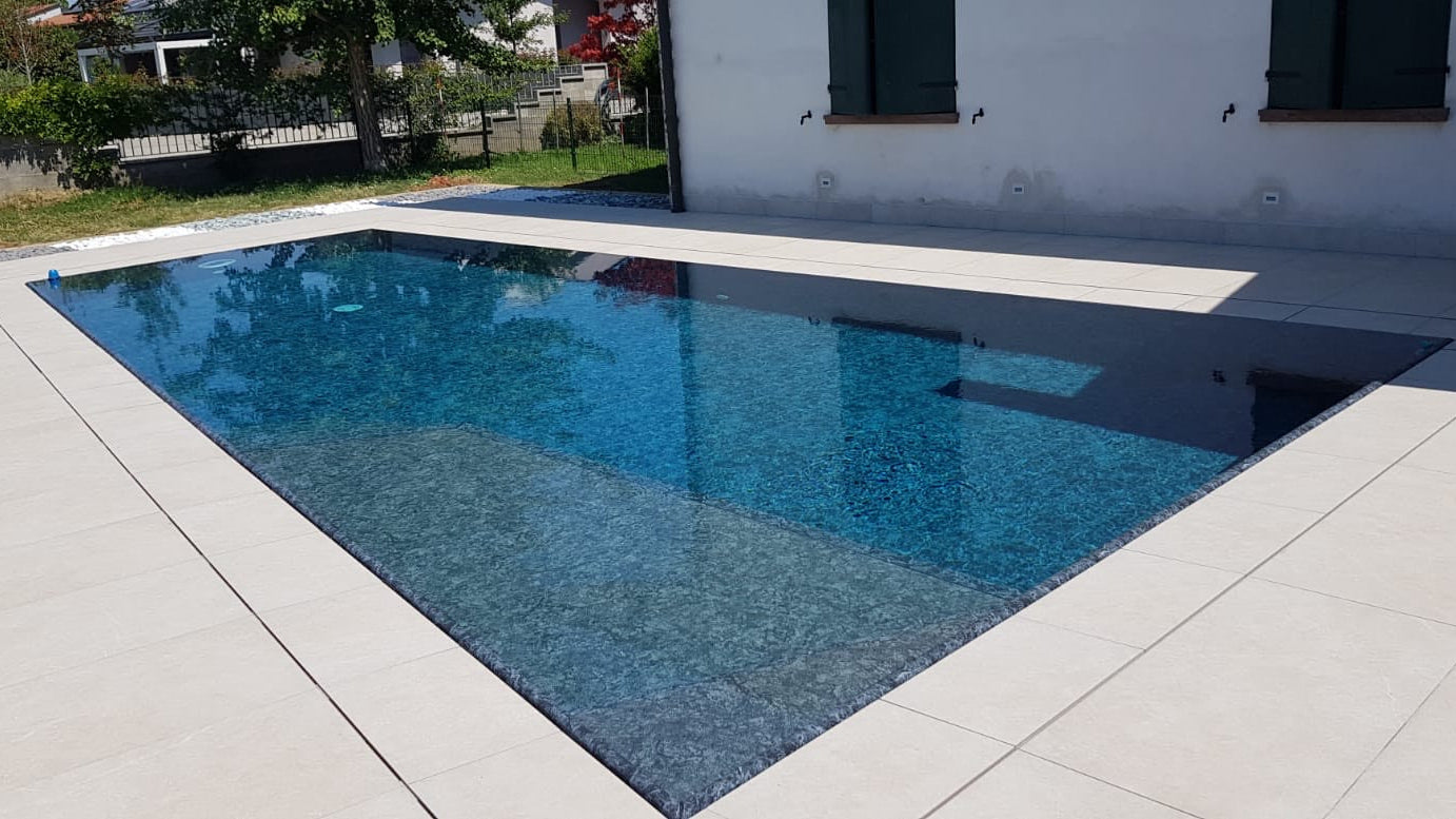 piscina con forma asimmetrica a sfioro con rivestimento scuro e spiaggia interna