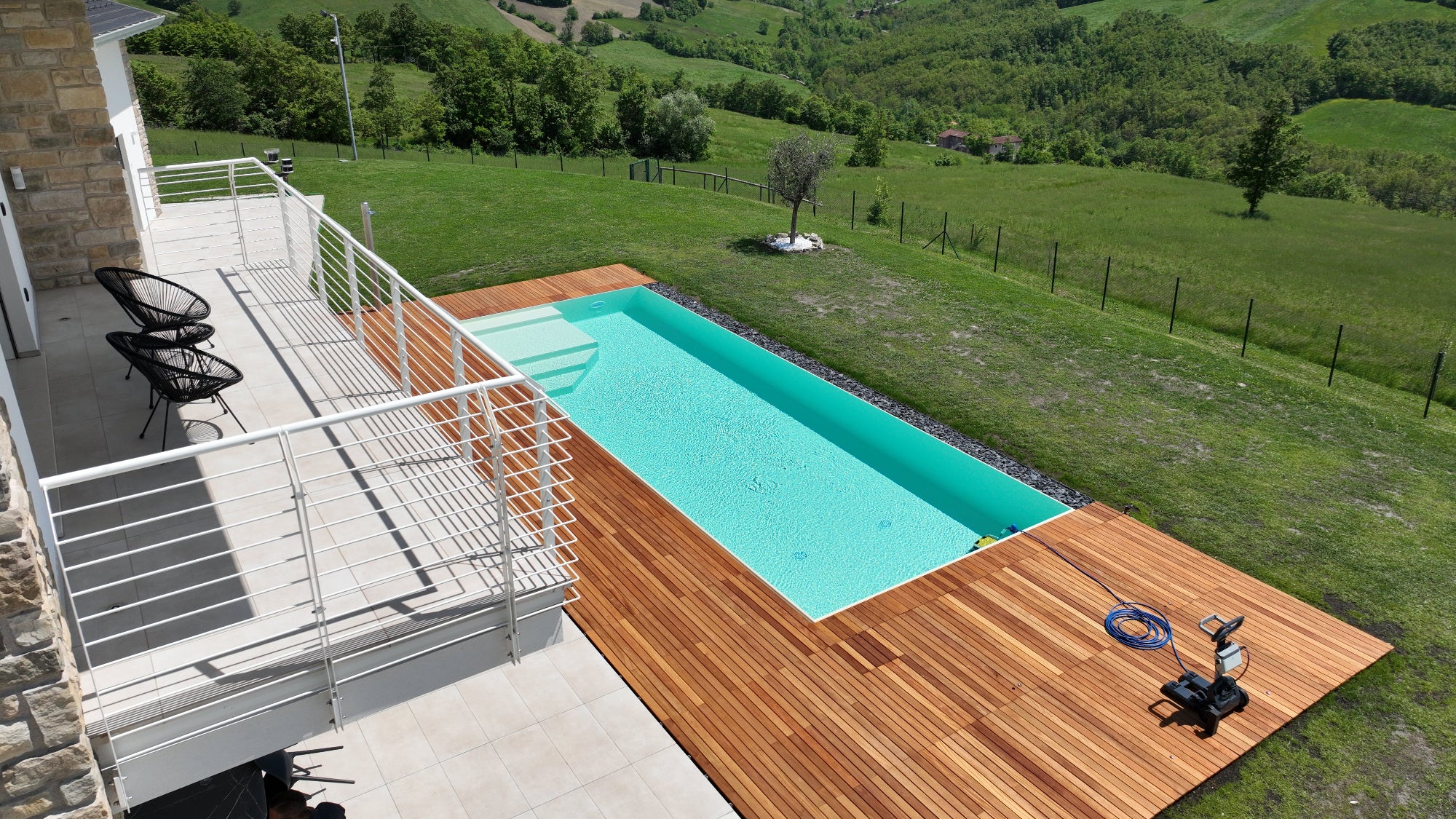 piscina rettangolare a sfioro senza vasca di compenso con spiaggia interna color sabbia e vaschette inox con sassi decorativi color ardesia, pavimento in legno