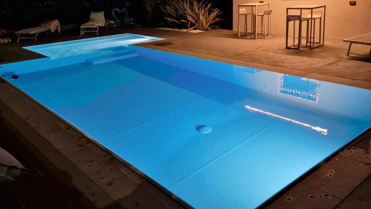 piscina rivestita con colore bianco con spiaggia angolare esterna a Rivalta sul Mincio ristrutturazione dettaglio sfioro di notte illuminata