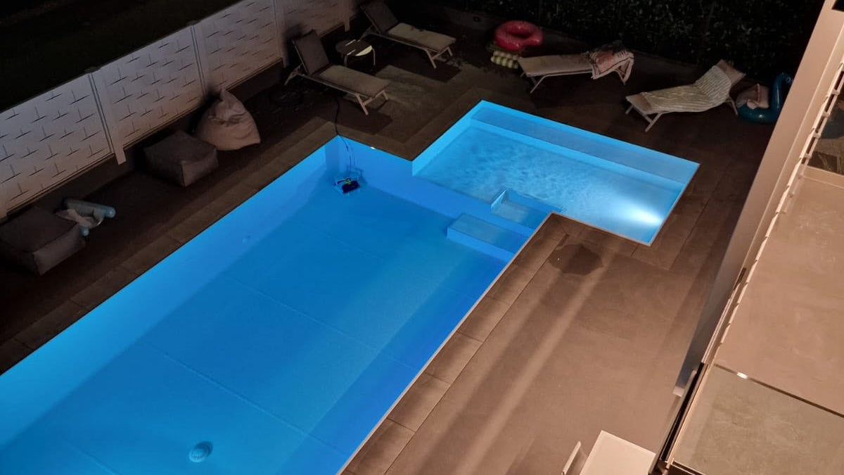 piscina rivestita con colore bianco con spiaggia angolare esterna a Rivalta sul Mincio ristrutturazione dettaglio sfioro di notte illuminata con fari bianchi
