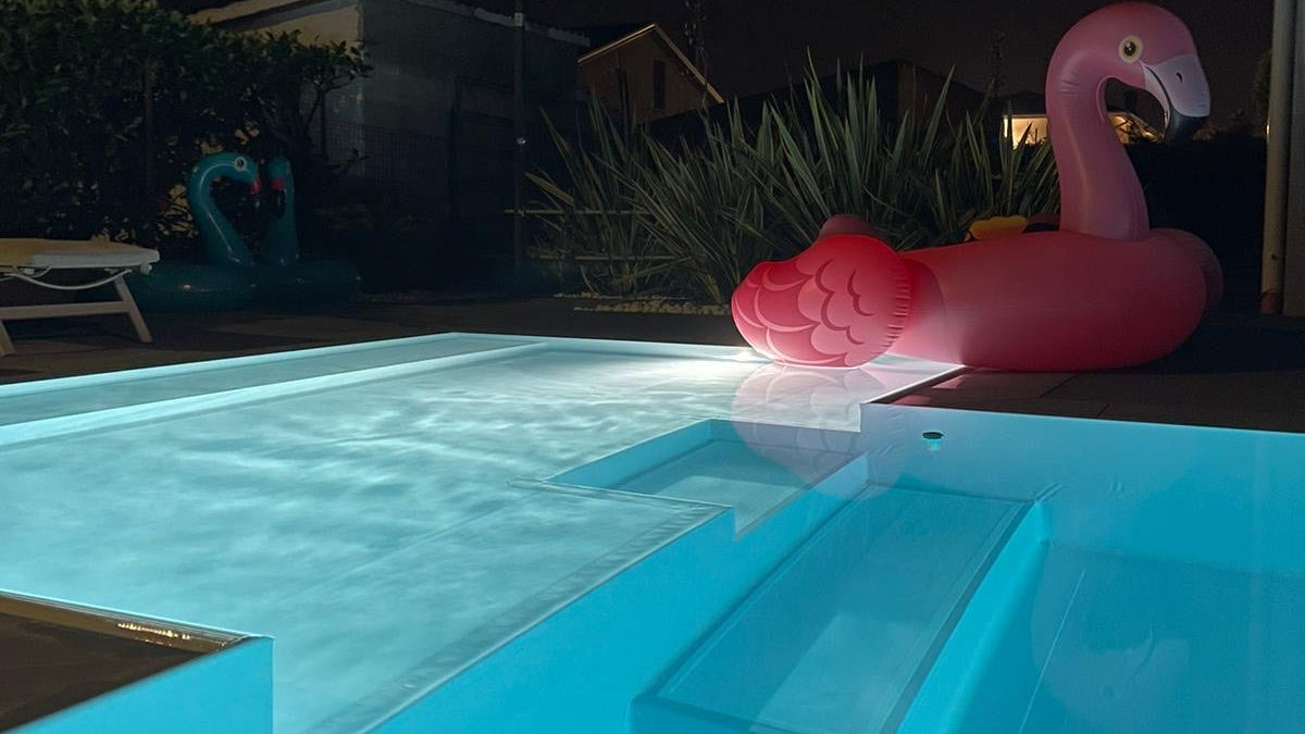 piscina rivestita con colore bianco con spiaggia angolare esterna a Rivalta sul Mincio ristrutturazione dettaglio sfioro di notte illuminata con fari bianchi proiettori  angolo relax