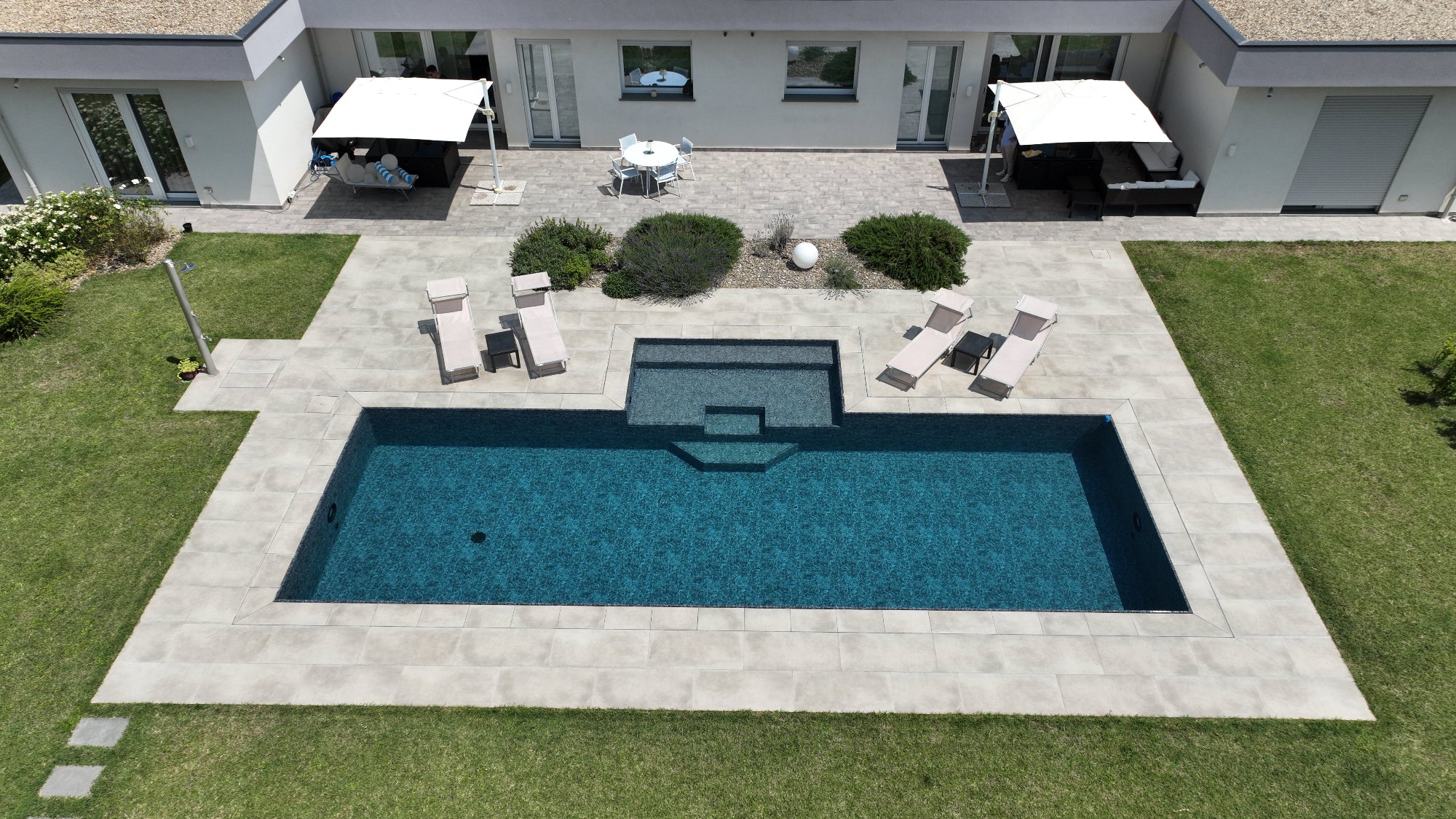 piscina sfioro rettangolare con spiaggia centrale esterna dal design moderno e accattivante, rivestimento effetto marmo nero a Reggio Emilia