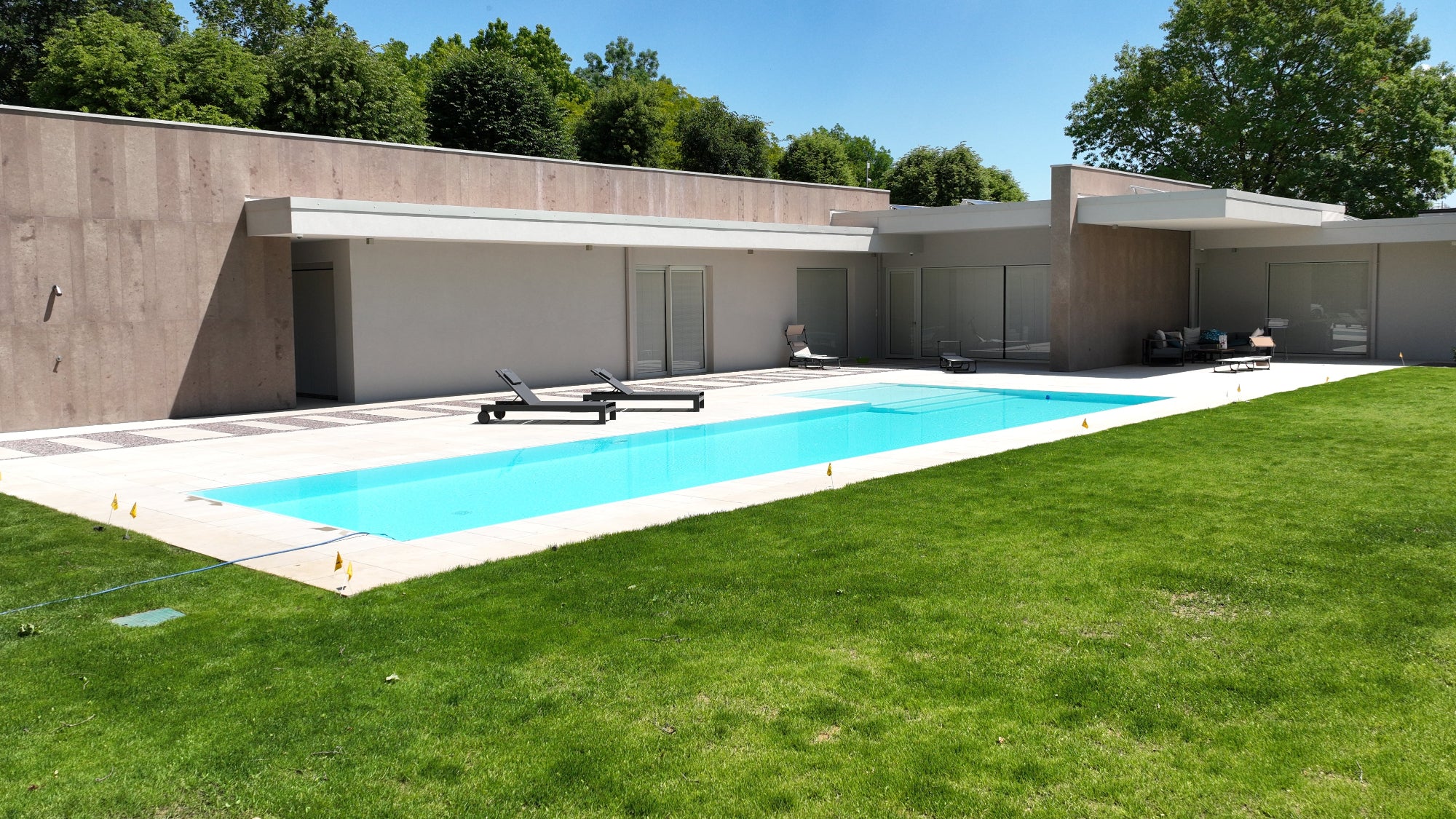 piscina sfioro senza vasca di compenso dal design elegante e moderno in linea con la casa, bagnasciuga esterno ad elle rivestimento bianci 