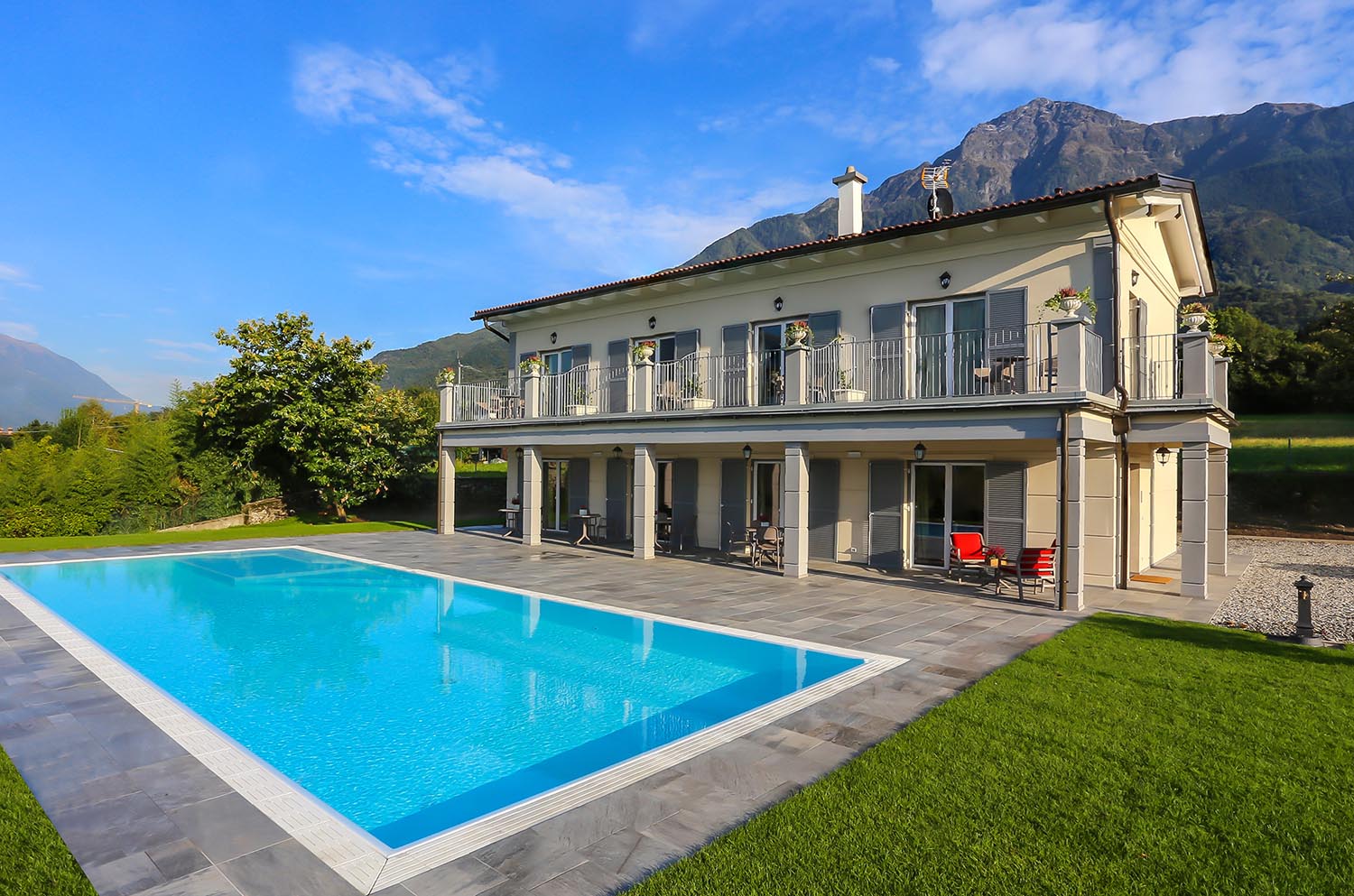 Casa riflessa su piscina a sfioro antisismica con liner bianco e griglia in pietra naturale. Piscina a sfioro con ingresso di design.
