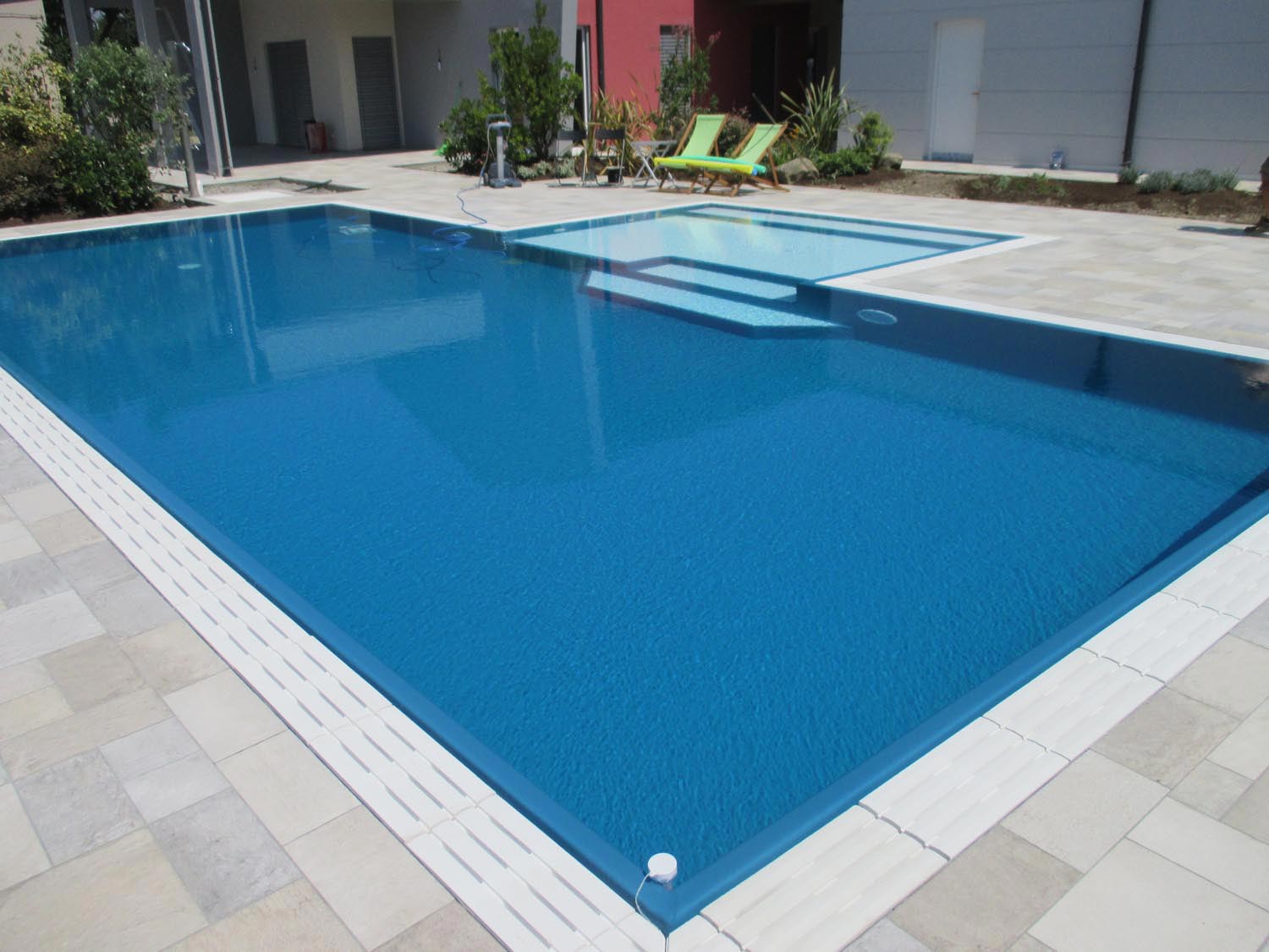 Vista totale di una piscina isotermica senza vasca di compensazione con griglia in pietra ricostruita bianca.