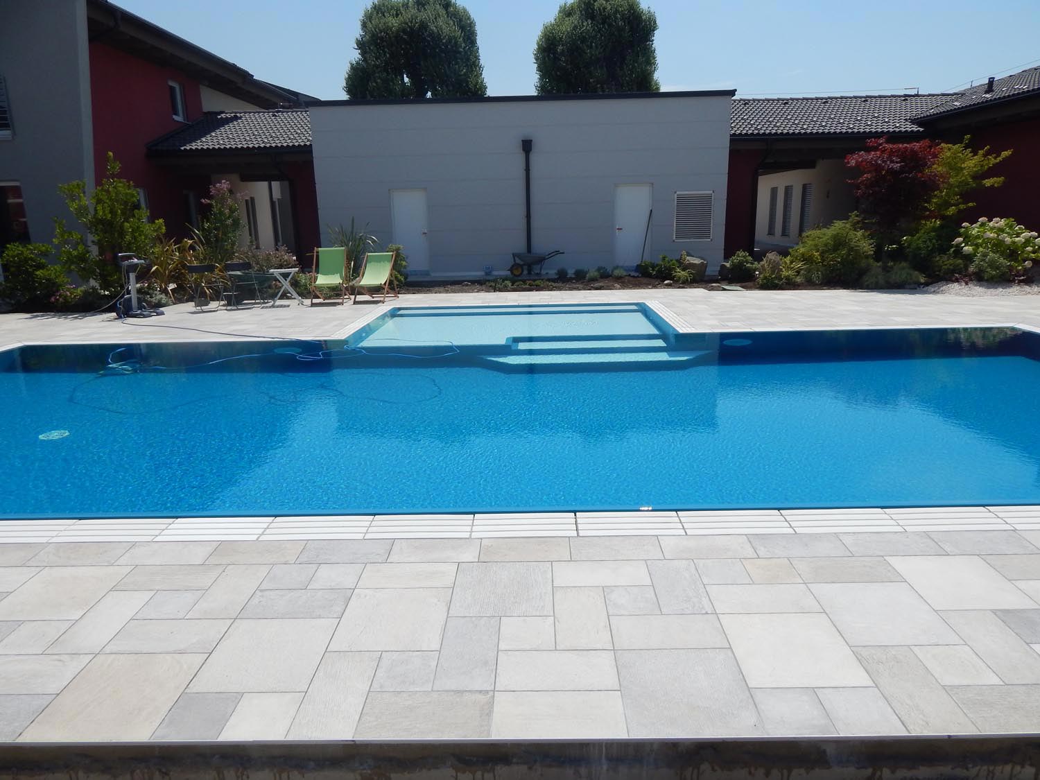 Panoramica di una piscina a sfioro senza vasca di compensazione blu perfetta per il nuoto. Piscina con bagnasciuga centrale perfetto per il riposo.