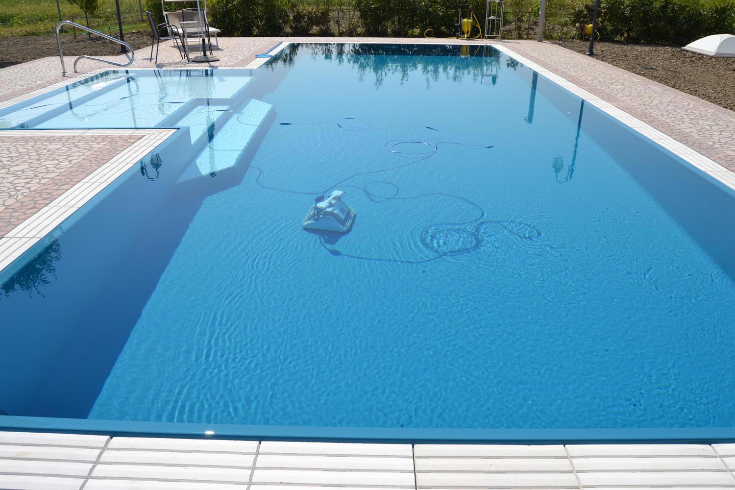 Robot piscina Dolphin Maxi durante la pulizia di una piscina a sfioro senza vasca di compenso ad altissima resa. Piscina adatta ad ospitare il robot grazie agli scalini di 50cm.