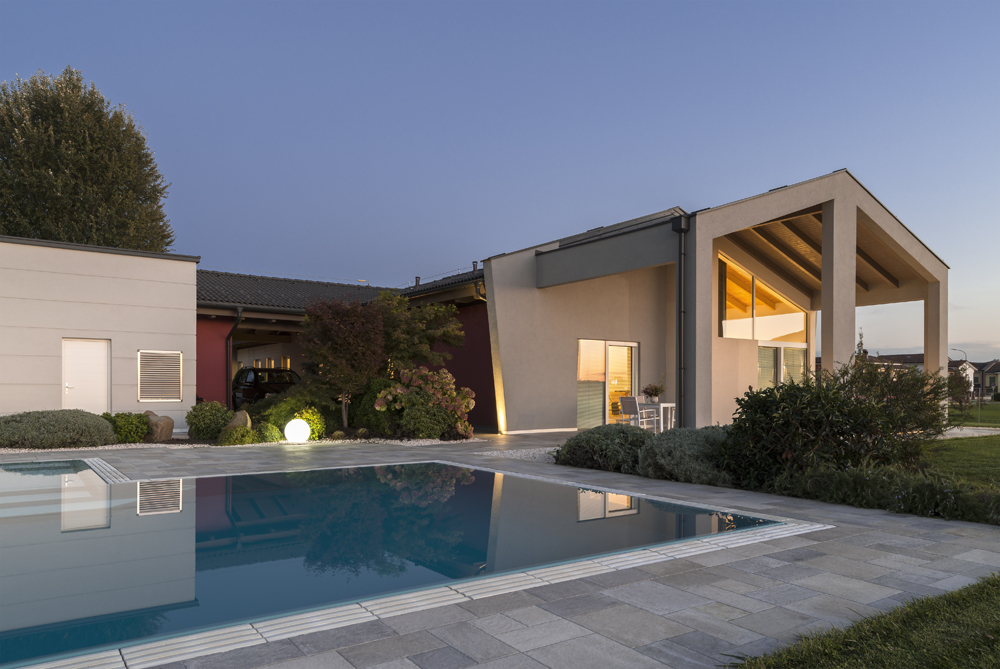Casa riflessa su piscina a sfioro senza vasca di compenso con griglia in pietra naturale.