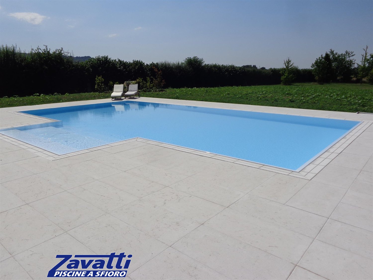 Vista completa di una piscina a sfioro autopulente Zavatti rifinita con griglia in pietra naturale bianca a una fessura
