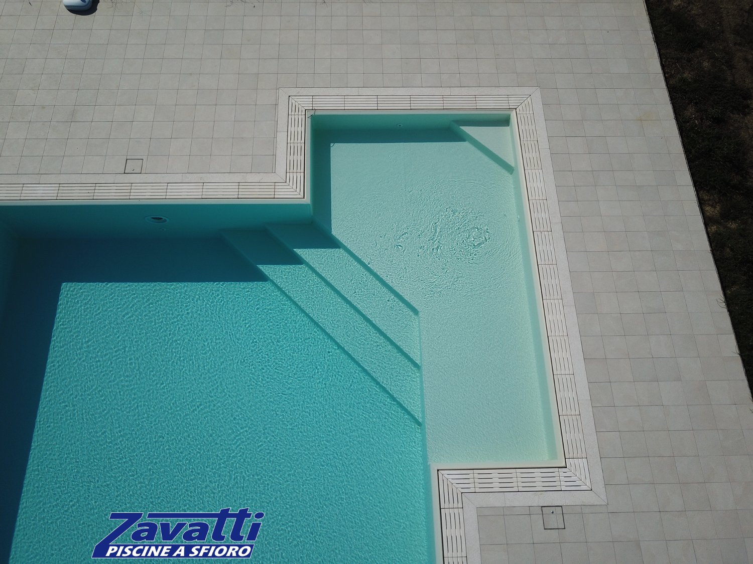 Dettaglio ingresso angolare di una piscina a sfioro con griglia in pietra ricostruita e rivestimento in PVC sabbia